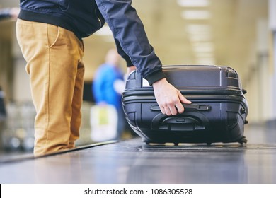 Traveler picking up suitcase from baggage claim in airport terminal. - Shutterstock ID 1086305528