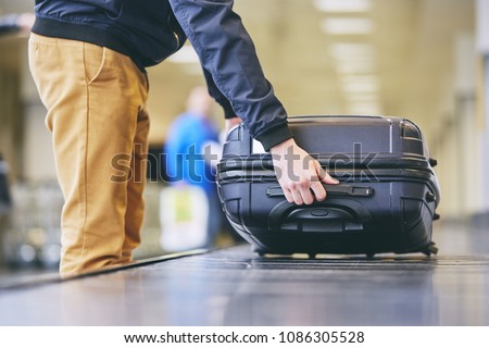 Traveler picking up suitcase from baggage claim in airport terminal.