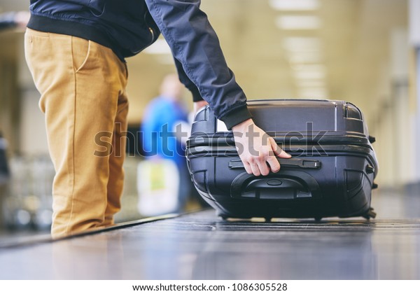 Traveler picking up suitcase from baggage claim\
in airport terminal.