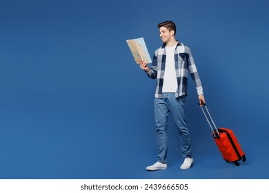 Traveler sideways fun man wear shirt casual clothes hold suitcase bag read map isolated on plain blue background. Tourist travel abroad in free spare time rest getaway Air flight trip journey concept