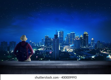 A traveler sitting on the rooftop watching at the city at night