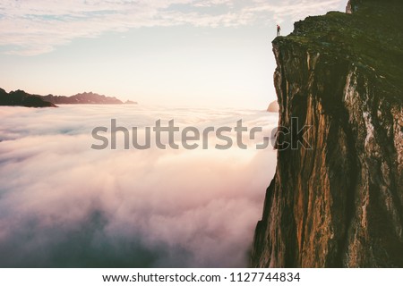 Traveler standing on cliff edge mountain top above sunset clouds travel adventure lifestyle summer journey vacations 