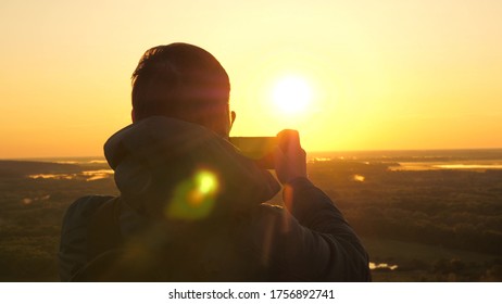 traveler takes photos and videos on his smartphone at dawn, from the mountain in rays of the beautiful sun. A free peasant tourist enjoys a beautiful view of nature from a high hill. travel concept - Shutterstock ID 1756892741