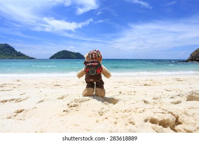 Traveler Teddy Bear Standing On Sand Beach , Background Mountain And Blue Sky By The Sea