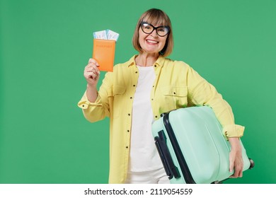Traveler tourist elderly fun woman in yellow shirt glasses hold suitcase valise passport ticket isolated on plain green background Passenger travel abroad on weekend getaway Air flight journey concept