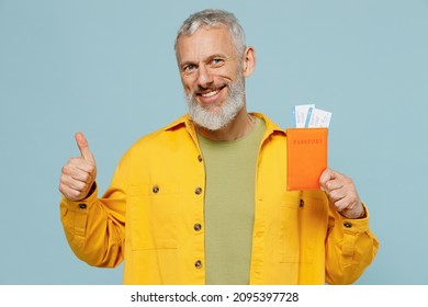 Traveler tourist elderly gray-haired bearded man in shirt hold passport ticket show thumb up isolated on plain blue background. Passenger travel abroad on weekends getaway. Air flight journey concept