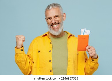 Traveler tourist elderly gray-haired bearded man in shirt hold passport ticket do winner gesture isolated on plain blue background. Passenger travel abroad weekends getaway. Air flight journey concept