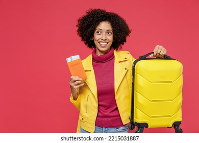 Traveler Tourist Fun Young Curly Black Latin Woman 20s Wears Yellow Jacket Hold Suitcase Bag Passport Boarding Tickets Isolated On Plain Red Background Studio Portrait. Passenger Travel Abroad Getaway