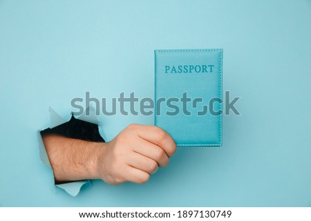 Traveler tourist man hand hold passport from a torn hole in blue paper