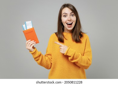Traveler tourist surprised woman in knitted yellow sweater point index finger on passport tickets isolated on grey background. Passenger travel abroad on weekends getaway. Air flight journey concept