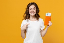 Traveler Tourist Woman 20s In White T-shirt Point Index Finger On Passport With Tickets Isolated On Yellow Orange Background. Passenger Traveling Abroad On Weekends Getaway. Air Flight Journey Concept