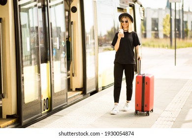 Traveler tourist woman in black casual clothes, sunglasses and hat with red suitcase use mobile phone to buy tickets online and sit on bus station. Female passenger travel abroad on weekends getaway