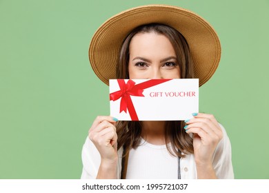 Traveler tourist woman in casual clothes hat camera cover mouth with gift voucher flyer mock up isolated on green background Passenger travel abroad on weekends getaway. Air flight journey concept.