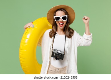 Traveler tourist woman in casual clothes hat sunglasses holding inflatable swim ring do winner gesture isolated on green background Passenger travel abroad weekend getaway Air flight journey concept.