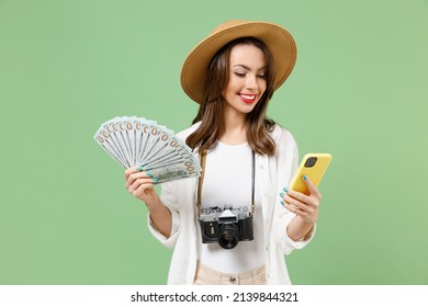 Traveler tourist woman in clothes hat hold mobile cell phone fan of cash money in dollar banknotes isolated on green background Passenger travel abroad on weekends getaway. Air flight journey concept