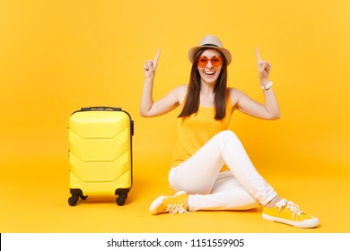 Traveler tourist woman in summer casual clothes hat sit with suitcase isolated on yellow orange background. Female passenger traveling abroad to travel on weekends getaway. Air journey concept Mock up