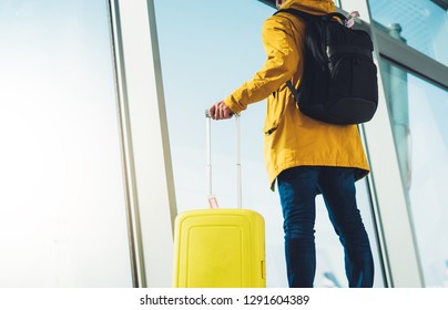 traveler tourist with yellow suitcase backpack is standing at airport on background large window, man in bright jacket wait in departure lounge area hall of ​ airport, vacation trip concept, mockup - Shutterstock ID 1291604389