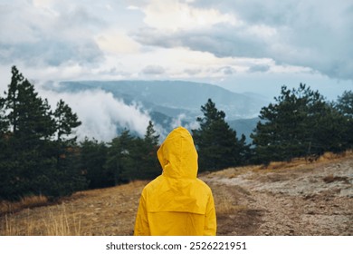 A traveler in a vibrant yellow raincoat admiring the majestic beauty of the mountains on a remote dirt road - Powered by Shutterstock