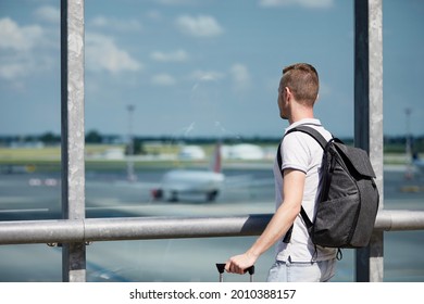 Traveler watching airplanes at airport. Rear view of passenger with backpack looking through window of terminal building.