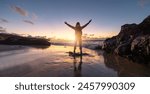 Traveler Woman with arms raised in triumph on a beach at sunset, silhouetted against vibrant sky and crashing waves. Travel and Freedom Concept image