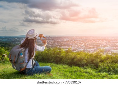 Traveler woman with backpack relaxing on hill top viewpoint and doing finger frame for crop the sun at sunset time, Hatyai viewpoint, Songkhla, Travel in Thailand, Summer holiday vacation travel trip
