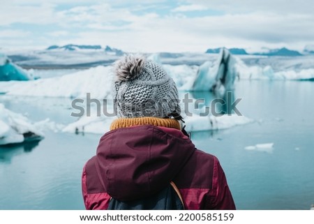 Traveler woman in cold weather clothes in front of the glaciers of Jökulsárlón in Iceland during a moody day filled with water. Live your dream, love in Iceland, road trip style.Copy space