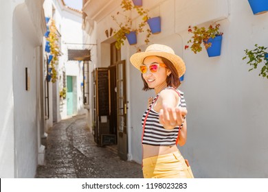 Traveler woman follow me to the famous white street with flowers in Andalusia, Spain