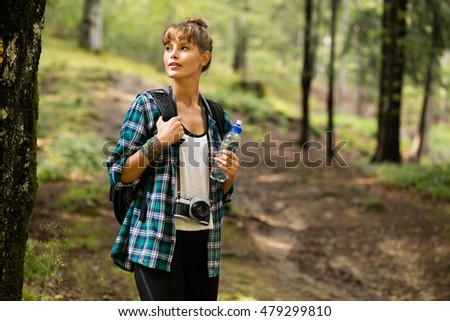 traveler woman in the middle of the forest walking with her backpack and bottle of water, discovering the nature around her