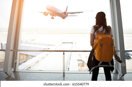 Traveler woman plan and backpack  see airplane flight at the airport glass window, girl tourist happy hold bag and waiting luggage in hall airplane departure.  Business people trip and Travel Concept
