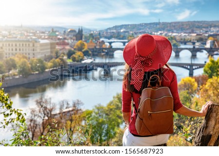 A traveler woman with red hat enjoys the elevated view over the city of Prague, Czech Republic, on a sunny autumn day