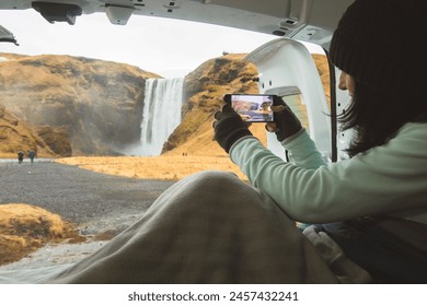 Traveler woman shoot video photo of beautiful waterfall use smartphone. Female tourist is taking photo with mobile phone camera while travel in Iceland stay in campervan by Skogafoss - Powered by Shutterstock
