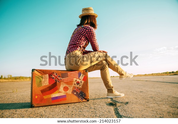 レトロなスーツケースに腰を下ろし 道路を見捨てる旅人女性 各国を表す切手旗の付いたスーツケースが旅行した の写真素材 今すぐ編集