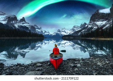 Traveler woman sitting on canoe with aurora borealis over Spirit Island in Maligne lake at Jasper national park, Alberta, Canada
