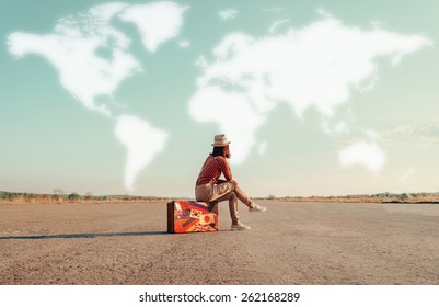 Traveler Woman Sitting On A Suitcase And Dreaming About Adventures. Map Of The World Is Painted In Sky. Concept Of Travel