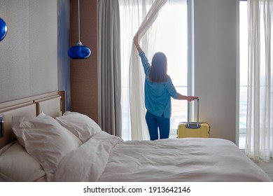 Traveler Woman With Suitcase Standing Near Window And Looking To A View From Hotel Room After Check-in. Conceptual Of Travel And Vacation Holiday