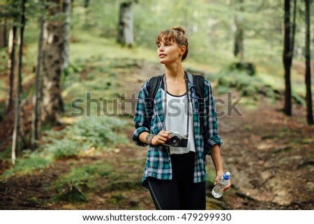 traveler woman walking into a forest with her backpack and looking for something to photograph