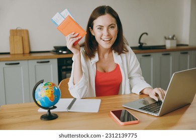 Traveler woman wear casual clothes hold passport ticket work on laptop pc computer near globe light kitchen at home. Tourist travel abroad in free time rest getaway. Air flight trip journey concept