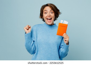 Traveler woman wear sweater hold passport ticket do winner gesture isolated on plain light blue cyan background Tourist travel abroad in free spare time rest getaway Air flight trip journey concept - Shutterstock ID 2253612525