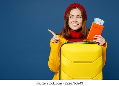 Traveler woman wears sweater red hat yellow raincoat hold suitcase passport ticket isolated on plain dark royal blue background Tourist travel abroad in free time rest getaway Air flight trip concept - Powered by Shutterstock