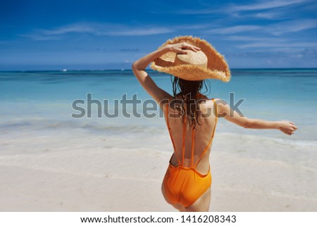 Traveler in a yellow bathing suit and a hat gesticulates with his hands and stands near the ocean                  