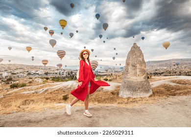 A travelers delight! A girl in a lovely dress watches the mesmerizing sight of the hot air balloons soaring high over the glorious landscape of Cappadocia, Turkey.