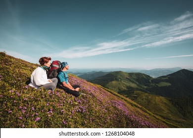 Travelers, friends relax on the mountain trail among flowering pink rhododendrons.  Adventure travel in the mountains. Back view, wide angle, vintage image. Cosmic atmosphere. - Shutterstock ID 1268104048