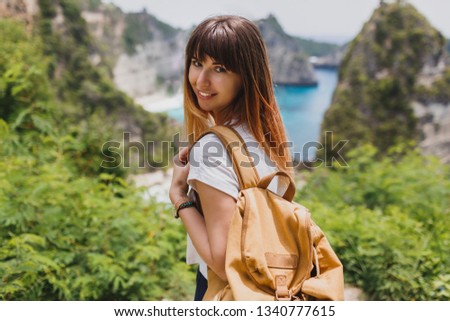 Traveling and adventure concept. Happy pretty woman with back pack  traveling in Indonesia on Nusa Penida island. Amazing cliffs and tropical beach view on background.