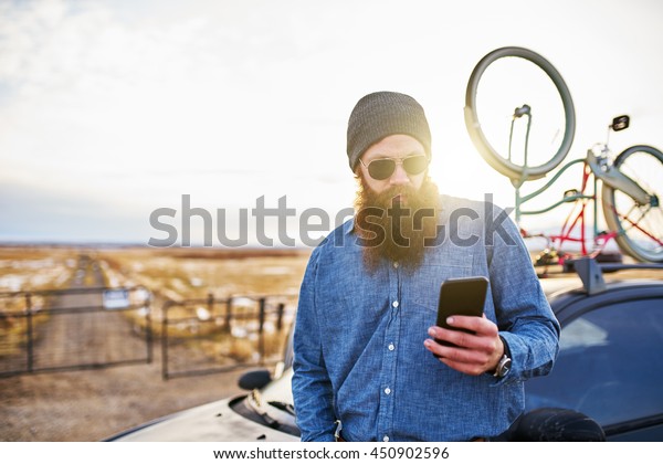 traveling bearded guy with bikes on his car\
using smart phone to look up\
directions
