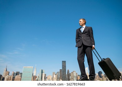 Traveling Businessman Standing With His Carry-on Wheelie Bag In Front Of The City Skyline