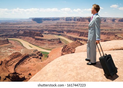 Traveling Businessman Standing With A Wheelie Carry-on Suitcase Looking Out Over Massive Red Rock Canyon Landscape