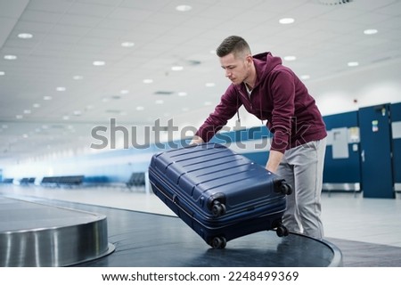 Traveling by airplane. Passenger pick up his blue suitcase in baggage claim in airport terminal.
