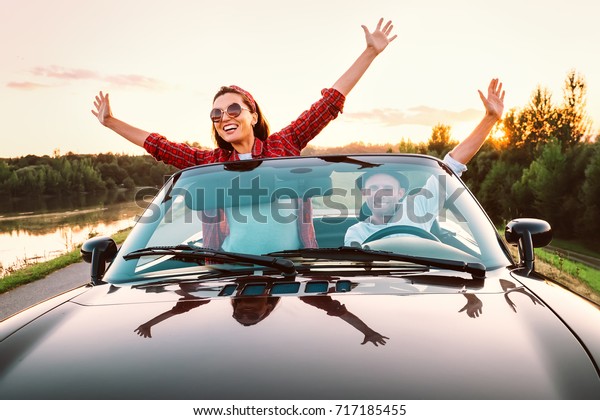 Traveling by car - happy couple in love go by\
cabriolet car in sunset\
time