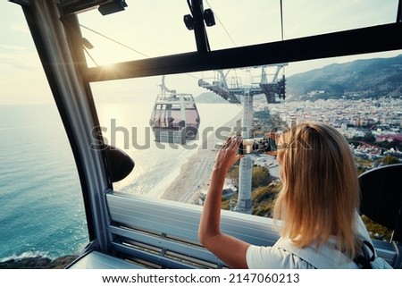 Traveling by Turkey. Young tourist woman sitting in Alanya's cable car enjoying view taking photo on her smartphone.
