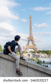 Traveling In Europe In Summer, A Man With Backpack Looking At Eiffel Tower, Famous Landmark And Travel Destination In Paris, France